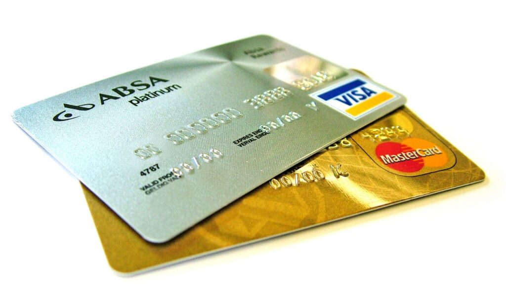 Close-up of silver Visa and gold MasterCard credit cards stacked on a white surface, used for travel reward redemptions.