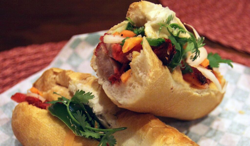 Close-up of a Vietnamese Banh Mi sandwich filled with grilled meat, pickled vegetables, fresh herbs, and sliced baguette.