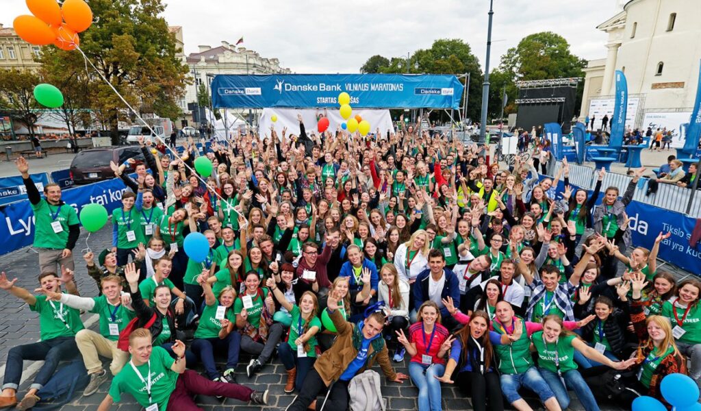 "Large group of cheerful volunteers posing at an outdoor event, symbolizing affordable travel through volunteering.