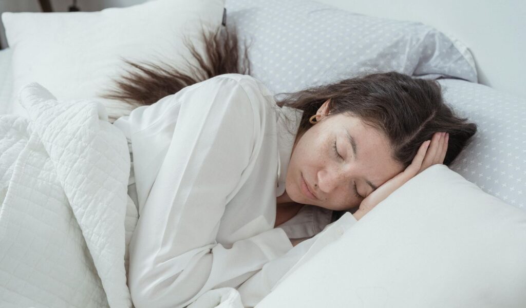 Woman peacefully sleeping in bed with white sheets and pillow, representing rest and overnight stays during travel.