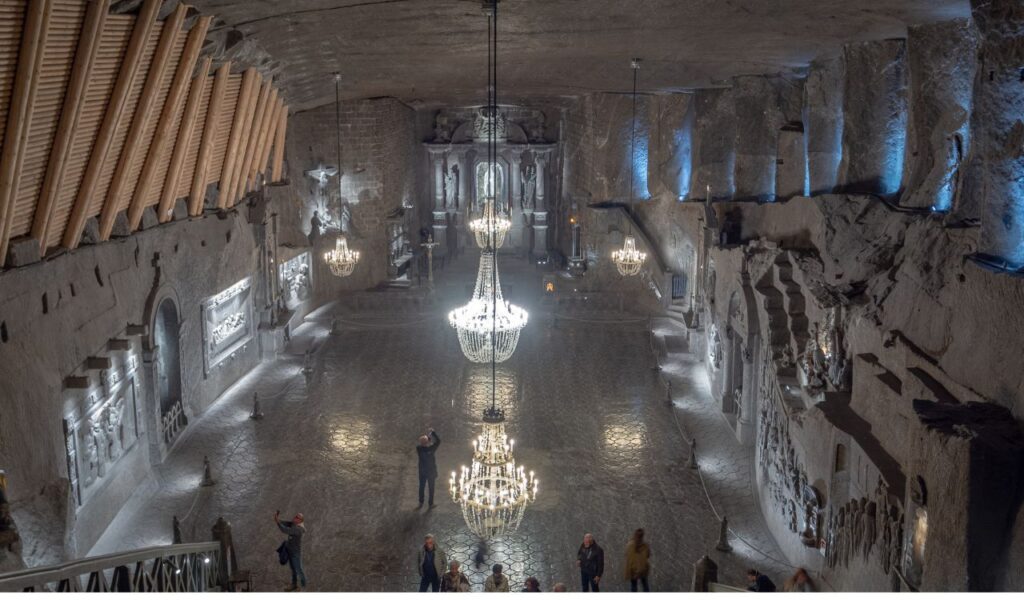 Grand underground chapel in Wieliczka Salt Mine, Poland, with chandeliers, salt carvings, and visitors.