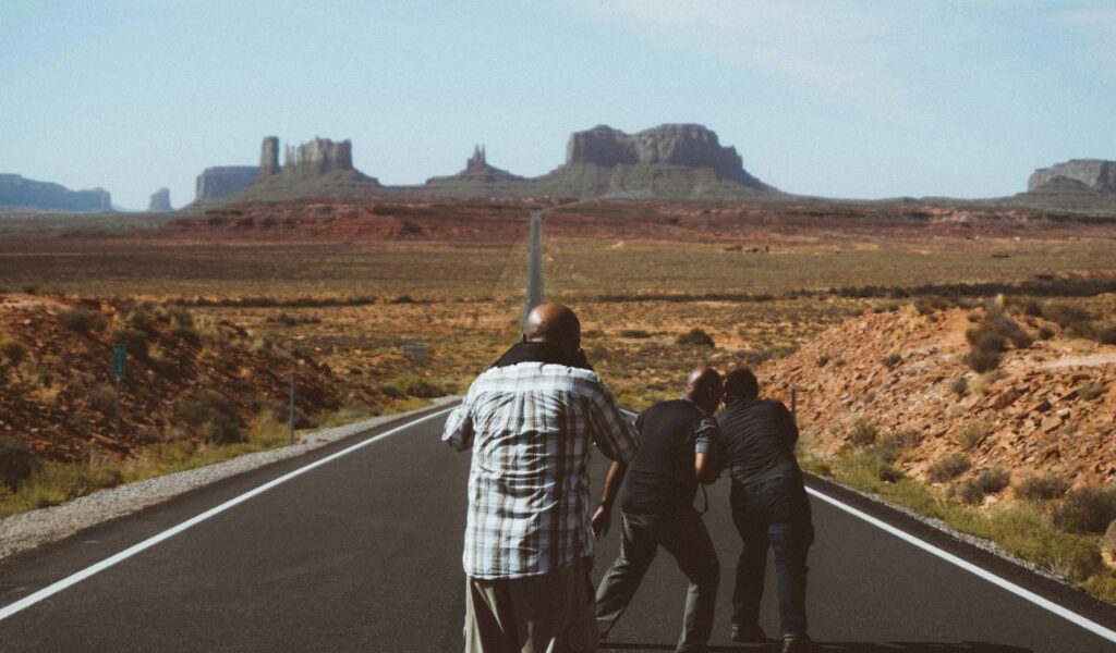 Group of people on a long desert highway photographing Monument Valley’s iconic rock formations in the distance.