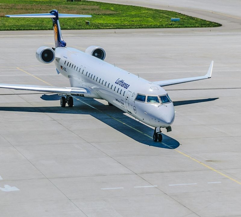 A Lufthansa airplane taxis on the runway as a ground crew member in orange directs its movement.