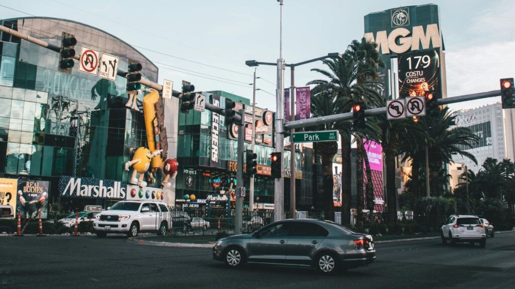 Lively Las Vegas Strip intersection with cars, palm trees, bright signs for Marshalls and MGM, and colorful M&M character statues.