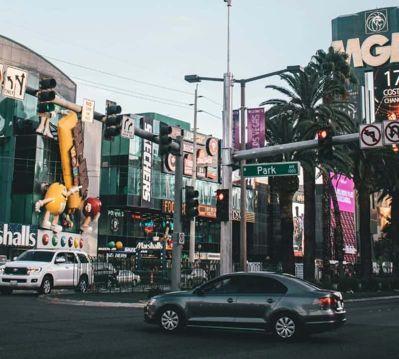Lively Las Vegas Strip intersection with cars, palm trees, bright signs for Marshalls and MGM, and colorful M&M character statues.