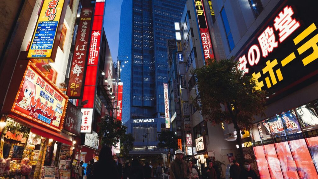 Busy street in Tokyo at night with bright neon signs, anime advertisements, and people walking below tall modern buildings.