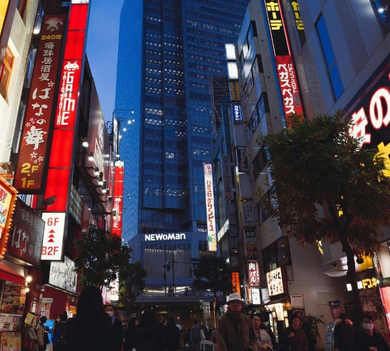 Busy street in Tokyo at night with bright neon signs, anime advertisements, and people walking below tall modern buildings.