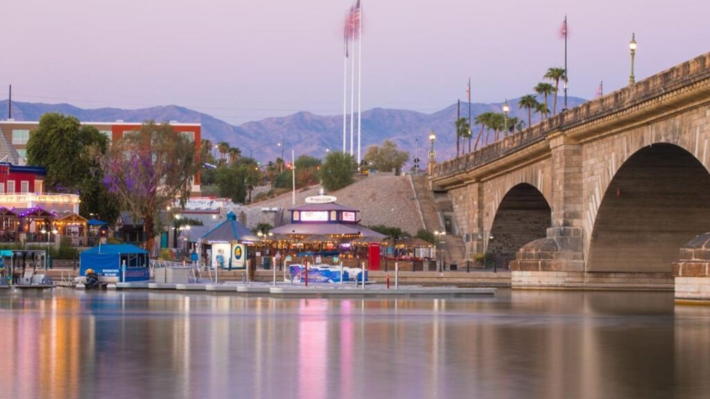 Scenic view of London Bridge in Lake Havasu City, Arizona, with waterfront restaurants, boats, and mountains at sunset.