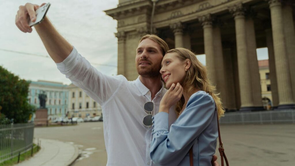 A couple taking a selfie together in front of a grand building with tall columns, smiling and enjoying their travel moment.