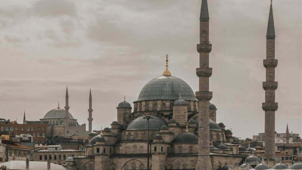 The New Mosque in Istanbul, Turkey, featuring its grand central dome, smaller surrounding domes, and two tall minarets under a cloudy sky.