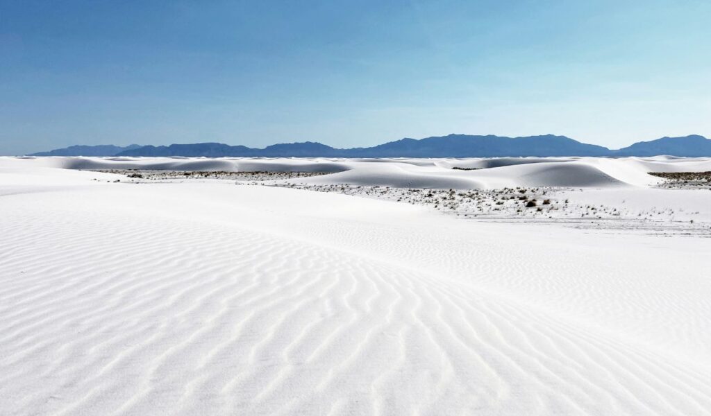 White gypsum sand dunes at White Sands National Park near Alamogordo, New Mexico, with rippled textures and distant mountains under a clear blue sky