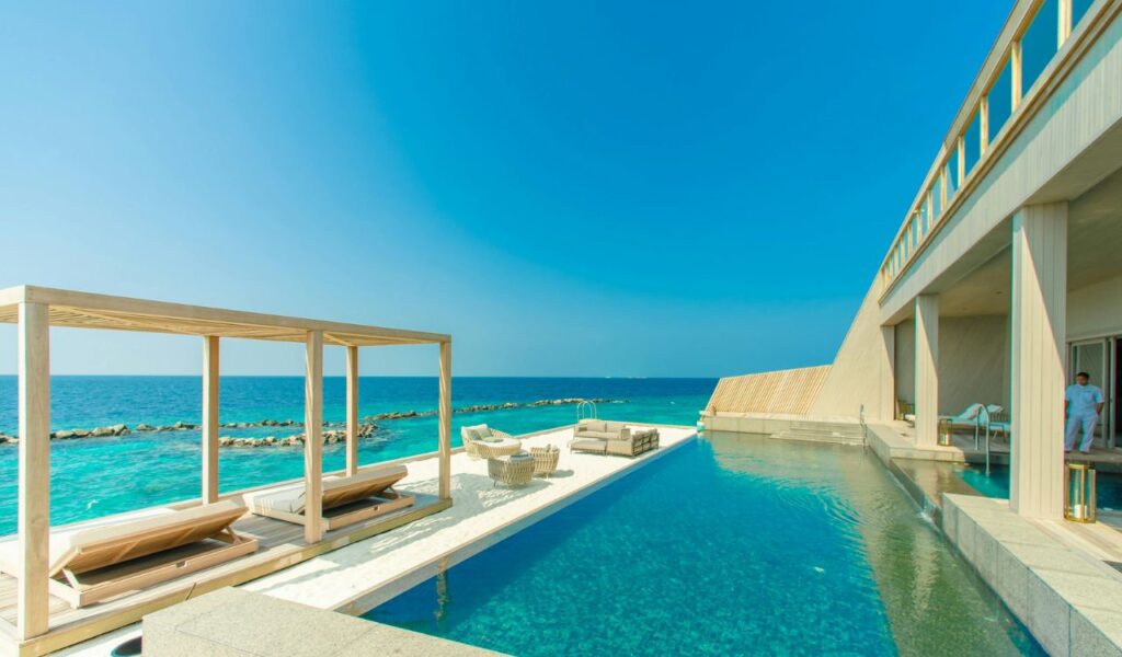 Luxury oceanfront villa with infinity pool, lounge chairs, and seating area overlooking turquoise sea.