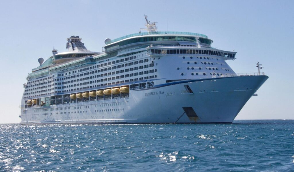 Large luxury cruise ship "Explorer of the Seas" sailing on a sunny day, with multiple decks, lifeboats, and passengers visible on board.