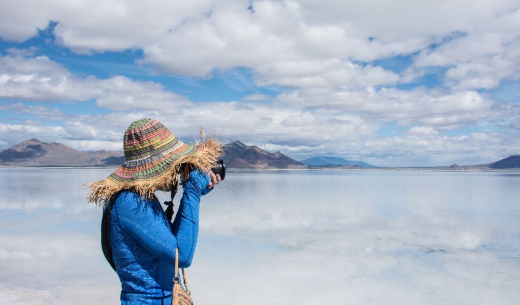 An adult female tourist wearing a straw hat wanders takes photos at the Bonneville Salt Flats in Utah. The salt flats are flooded with water.