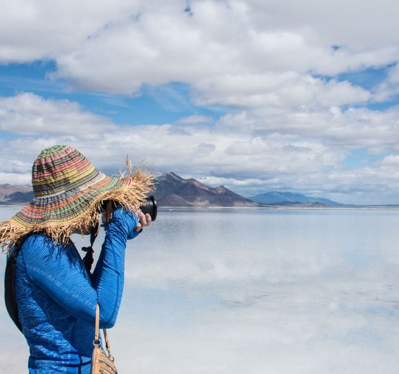 An adult female tourist wearing a straw hat wanders takes photos at the Bonneville Salt Flats in Utah. The salt flats are flooded with water.