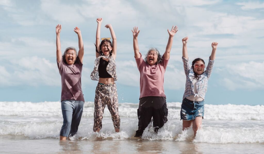 Asian multi generational family enjoying joyful moments on the beach. Happy women and daughter splashing water together, fun, bonding, and freedom across ages.