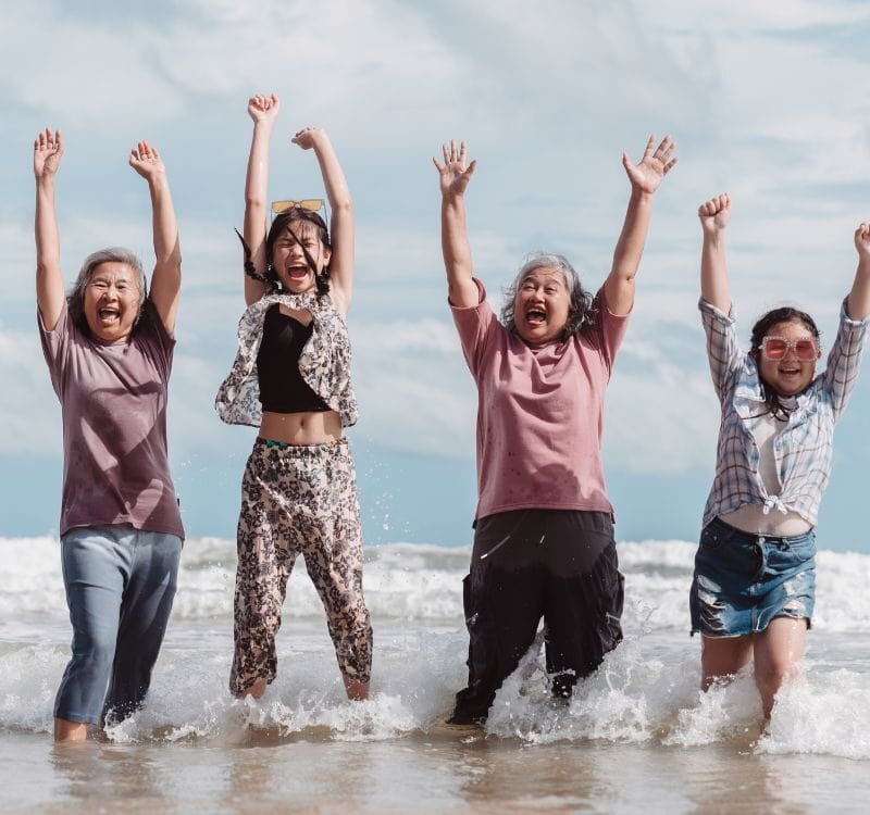 Asian multi generational family enjoying joyful moments on the beach. Happy women and daughter splashing water together, fun, bonding, and freedom across ages.