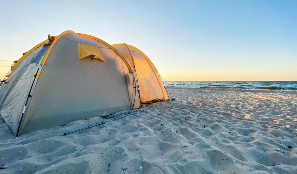A yellow and gray tent sits on sandy shores at Assateague Island, Maryland, with ocean waves and a clear blue sky during sunset.