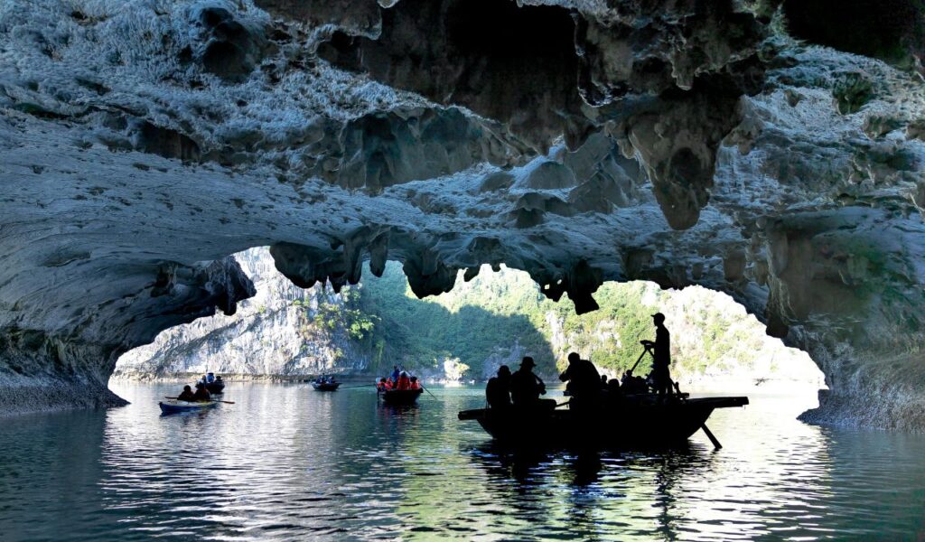 Boats with tourists paddle through the entrance of the Blue Grotto in Italy, surrounded by rocky cave walls and clear blue water.