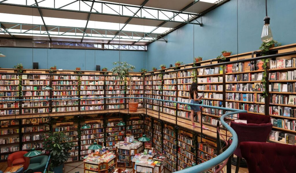 A woman browses books on the upper level of Cafebrería El Péndulo in Mexico City, surrounded by tall shelves and cozy seating.