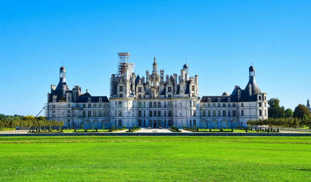 Chateau de Chambord in France, a grand Renaissance-style castle with ornate towers and detailed architecture, set against a clear blue sky and surrounded by manicured green lawns.