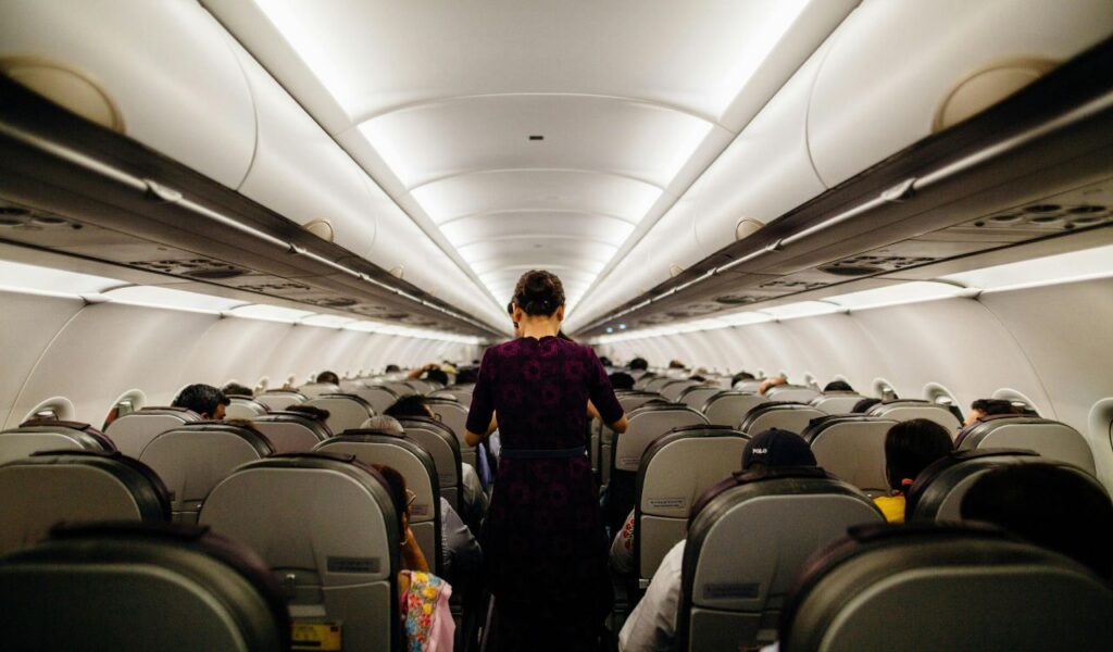 Flight attendant walks down airplane aisle as passengers sit on a budget flight with hidden fees.
