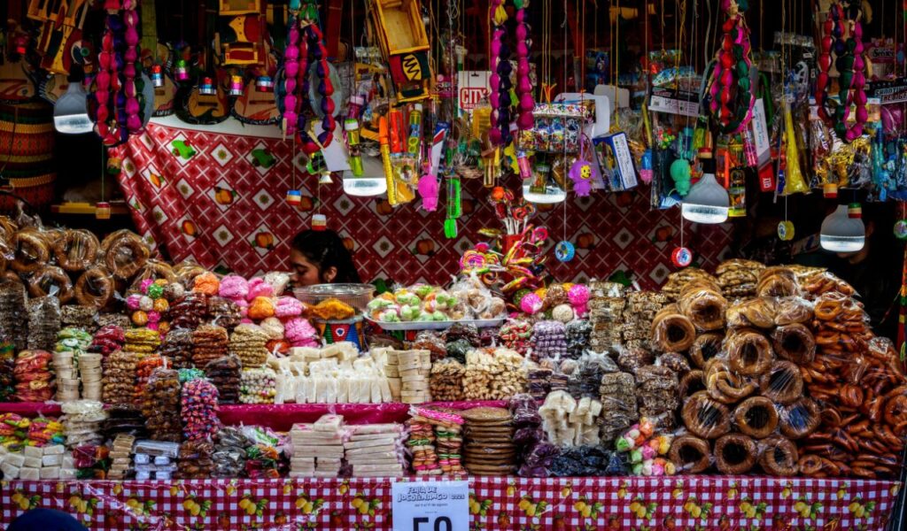 Colorful market stall in Guatemala selling assorted sweets, pastries, and toys, with a vendor partially hidden behind the display.