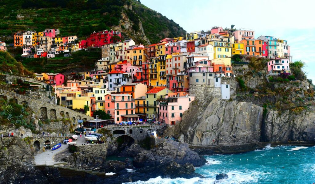 Colorful cliffside buildings of Cinque Terre, Italy, overlooking the turquoise Ligurian Sea, with rugged rock formations and scenic coastal views.