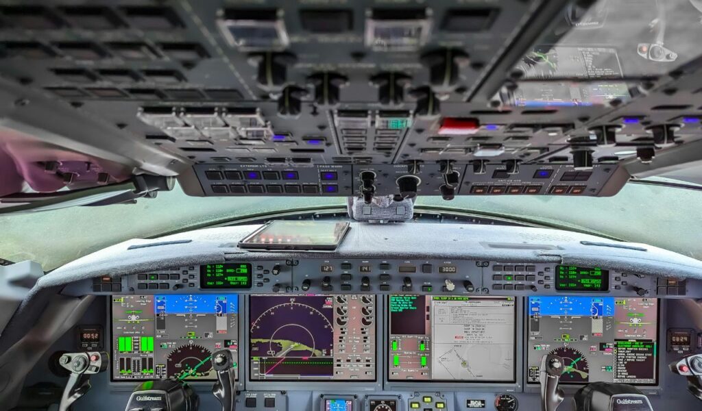 The cockpit of an airplane filled with illuminated control panels, digital screens displaying flight data, and steering yokes in view.
