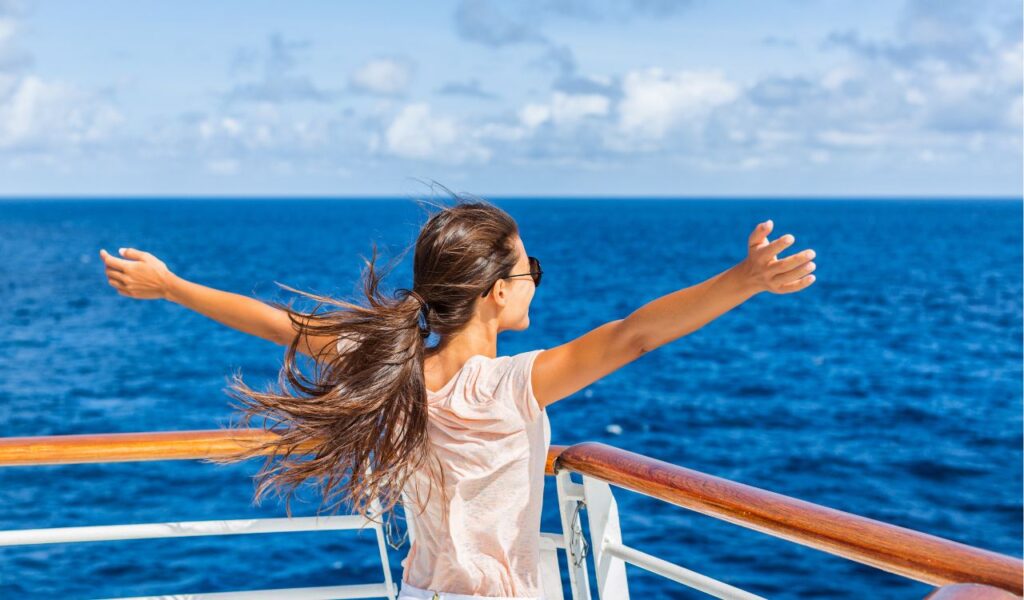 Cruise ship vacation woman enjoying travel vacation at sea. Free carefree happy girl looking at ocean with open arms in freedom pose.