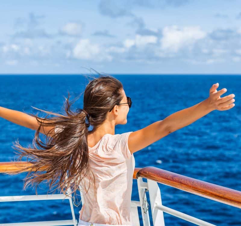 Cruise ship vacation woman enjoying travel vacation at sea. Free carefree happy girl looking at ocean with open arms in freedom pose.