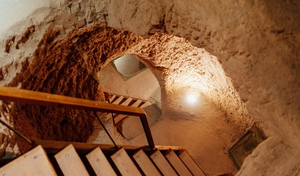 Wooden stairs descend into a narrow, dimly lit tunnel carved from reddish rock inside Derinkuyu Underground City in Turkey.