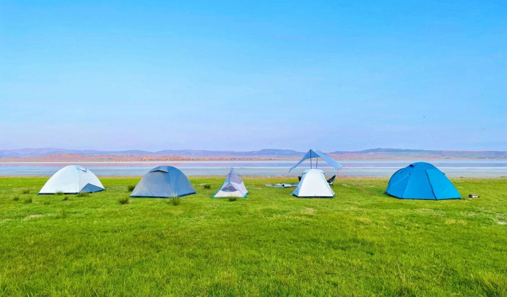 Tents are set up on a green lakeside field at Devil’s Lake State Park, Wisconsin, with calm waters and distant hills under a clear blue sky.