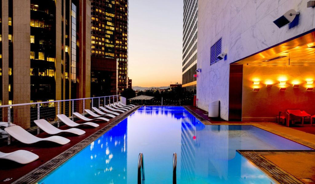 Rooftop hotel pool with lounge chairs and city skyscraper views at sunset in a remote urban location.
