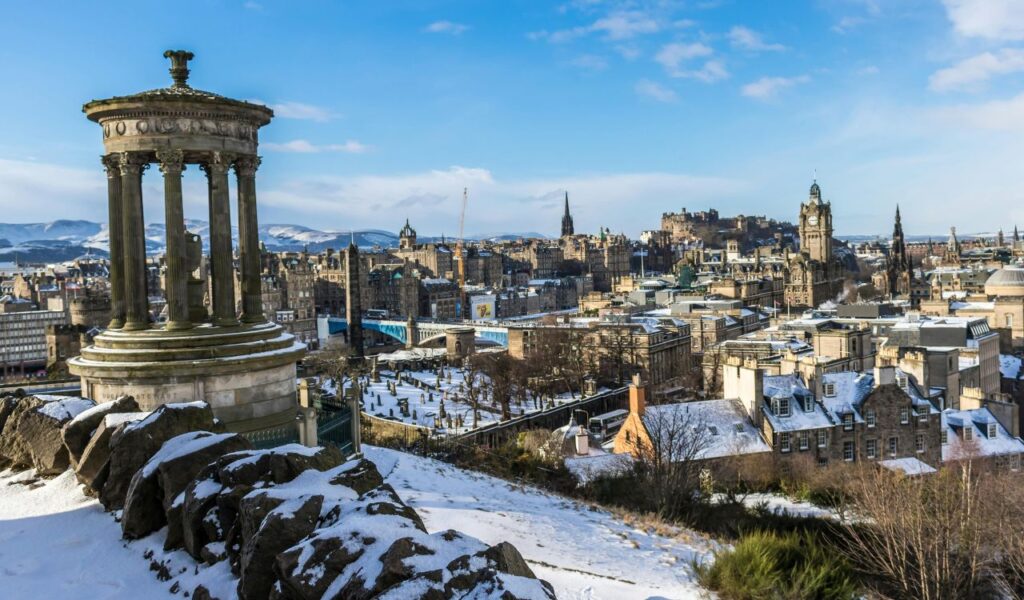 Snowy Edinburgh view from Calton Hill with the Dugald Stewart Monument and city skyline, including Edinburgh Castle.