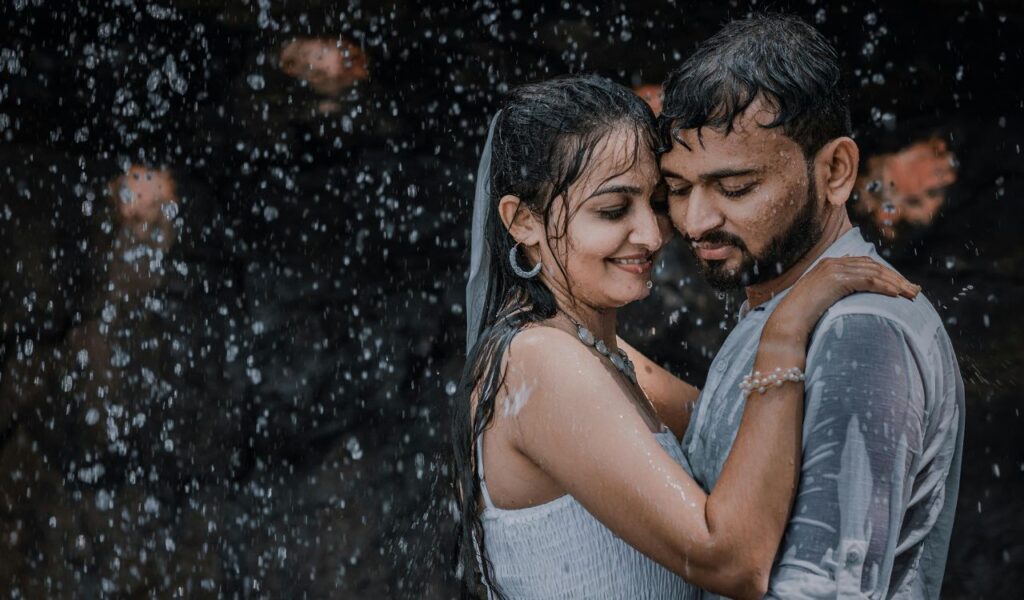 Couple embracing under falling water, smiling and enjoying the moment in rainy or moody weather.