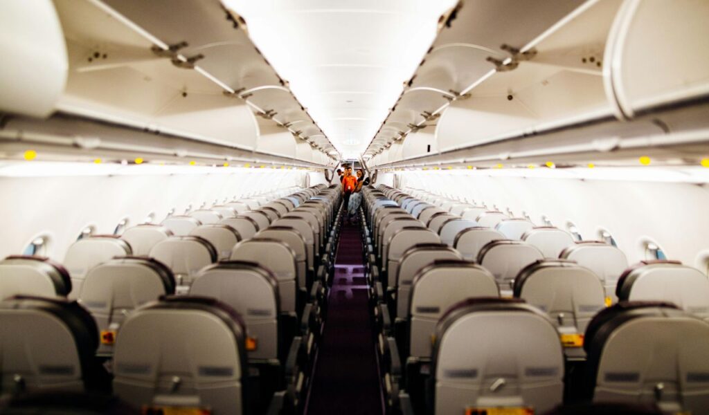 An empty airplane cabin with open overhead bins and neatly arranged seats, showing a clean and spacious interior with bright lighting.