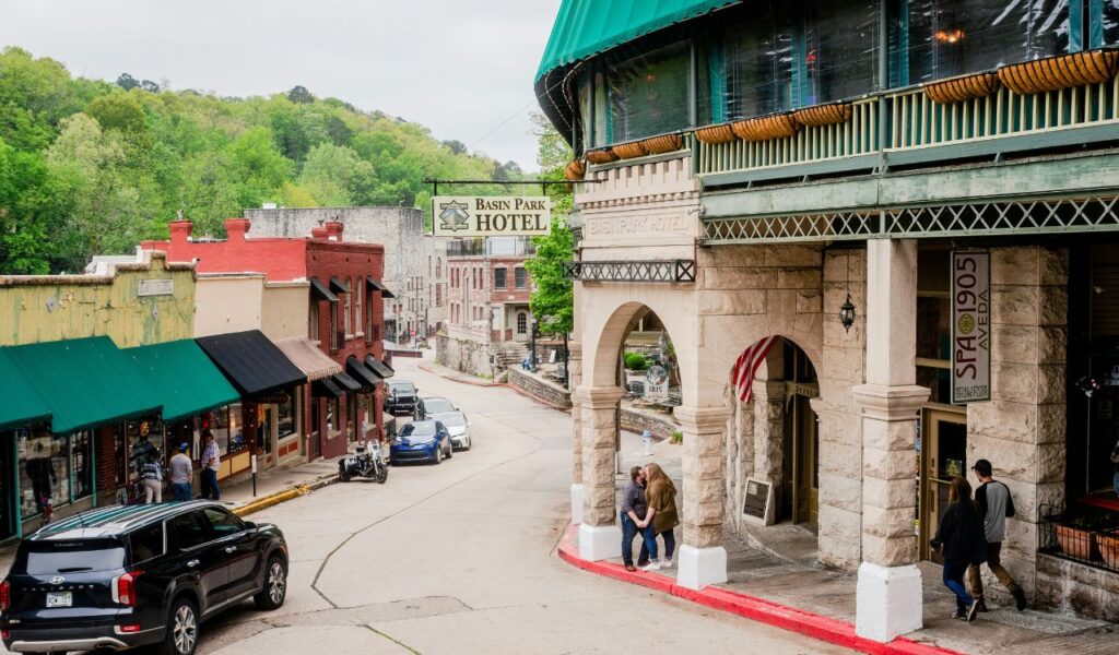 Downtown Eureka Springs, Arkansas, with historic buildings, colorful awnings, shops, and the Basin Park Hotel sign.