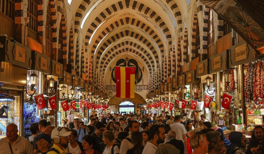  Crowded indoor market in Istanbul with Turkish flags hanging above stalls selling spices, lamps, and goods
