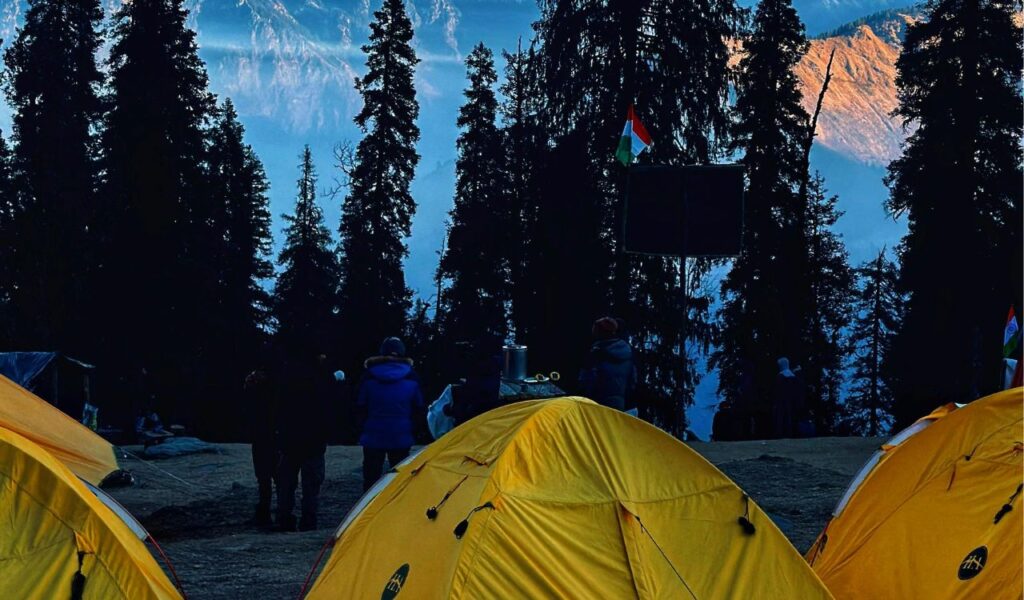 Yellow tents set up in a forested area of the Great Smoky Mountains, with campers bundled up and misty blue ridges visible in the background.
