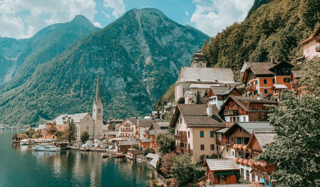 Picturesque lakeside village of Hallstatt, Austria, with charming alpine houses, a tall church spire, and towering mountains in the background.