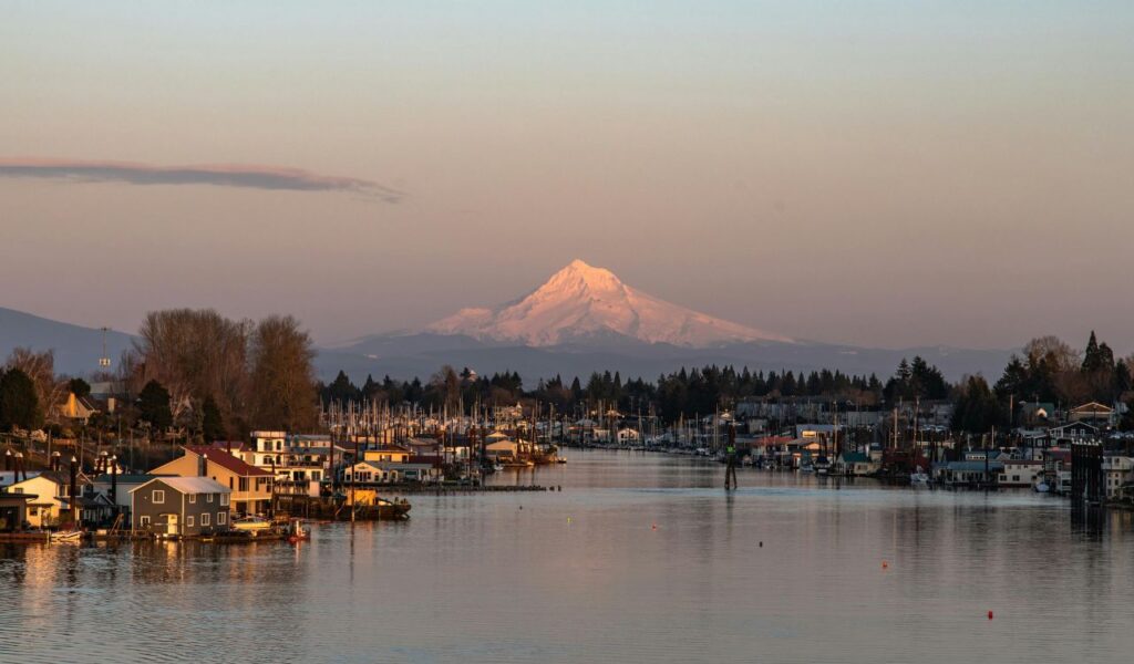 Snow-capped Mount Hood rises in the distance over the calm waters and marina of Hood River, Oregon, at sunset.