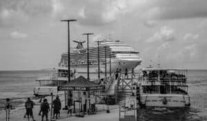 Passengers boarding a tender boat at a dock with the Carnival Dream cruise ship anchored in the background, preparing for departure.