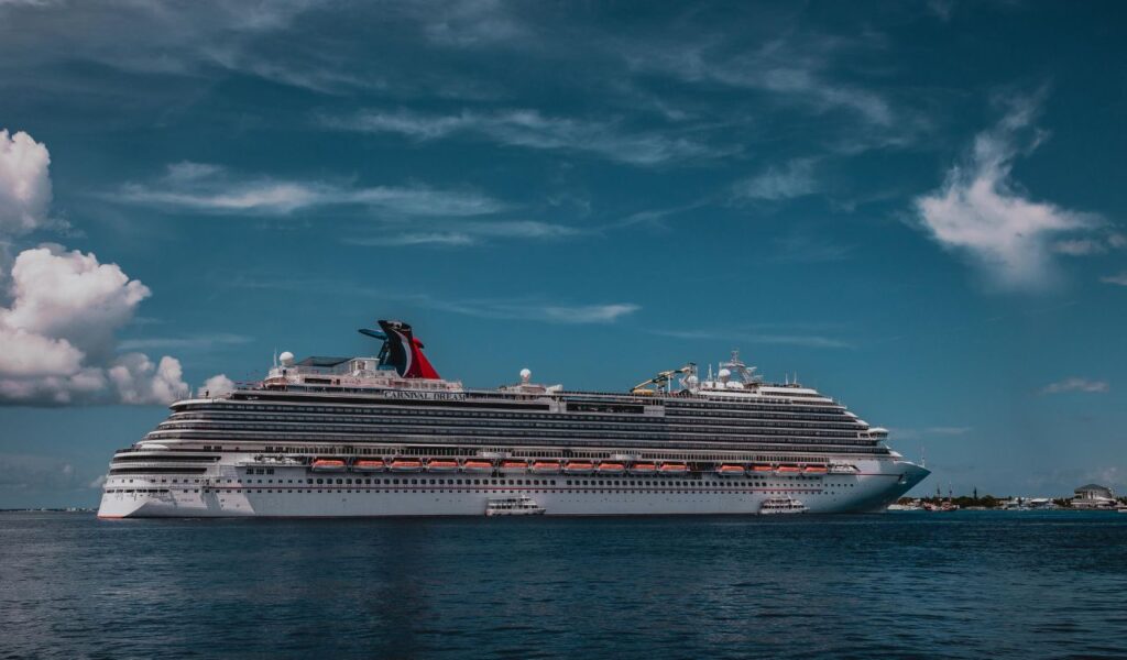 Large Carnival Dream cruise ship anchored near shore under a partly cloudy blue sky, with smaller boats nearby.