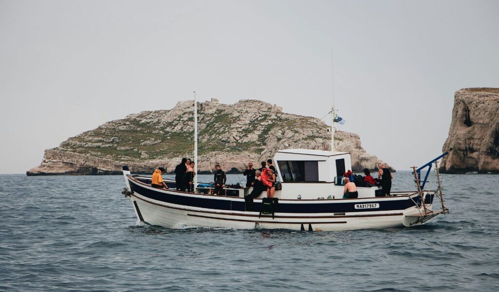 A group of people on a white and blue boat near rocky islands, preparing for a water activity on a calm sea under a gray sky