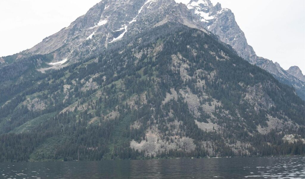 Snow-capped peaks tower above forested slopes and the calm waters of Jenny Lake in Wyoming’s Grand Teton National Park.