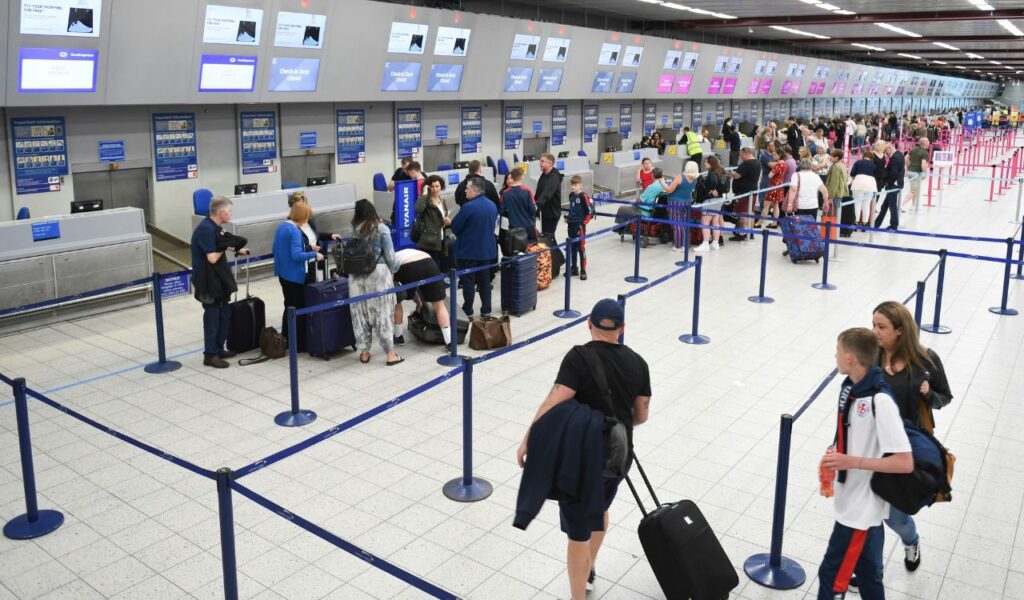 Passengers waiting in line at an airport check-in counter with luggage and travel documents