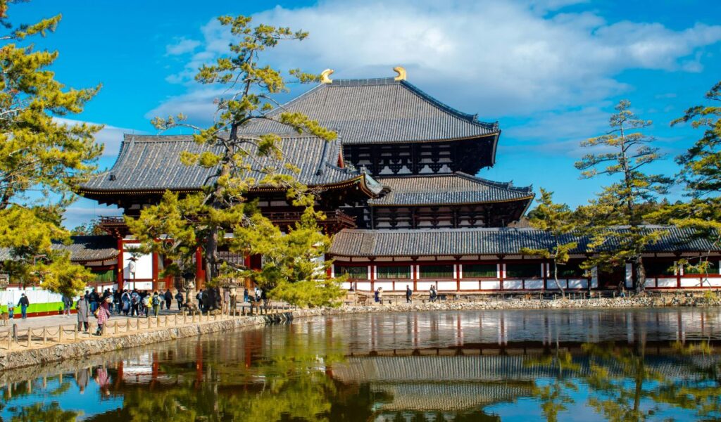 istoric view of Nijo Castle in Kyoto, Japan, with traditional Japanese architecture, surrounding trees, and a calm reflecting pond in front, visited by tourists.