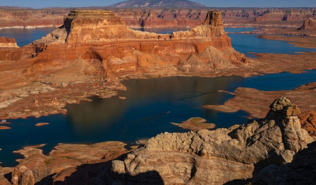 Lake Powell’s deep blue water winds between towering red rock formations, with boats cruising through the desert landscape of Arizona and Utah.