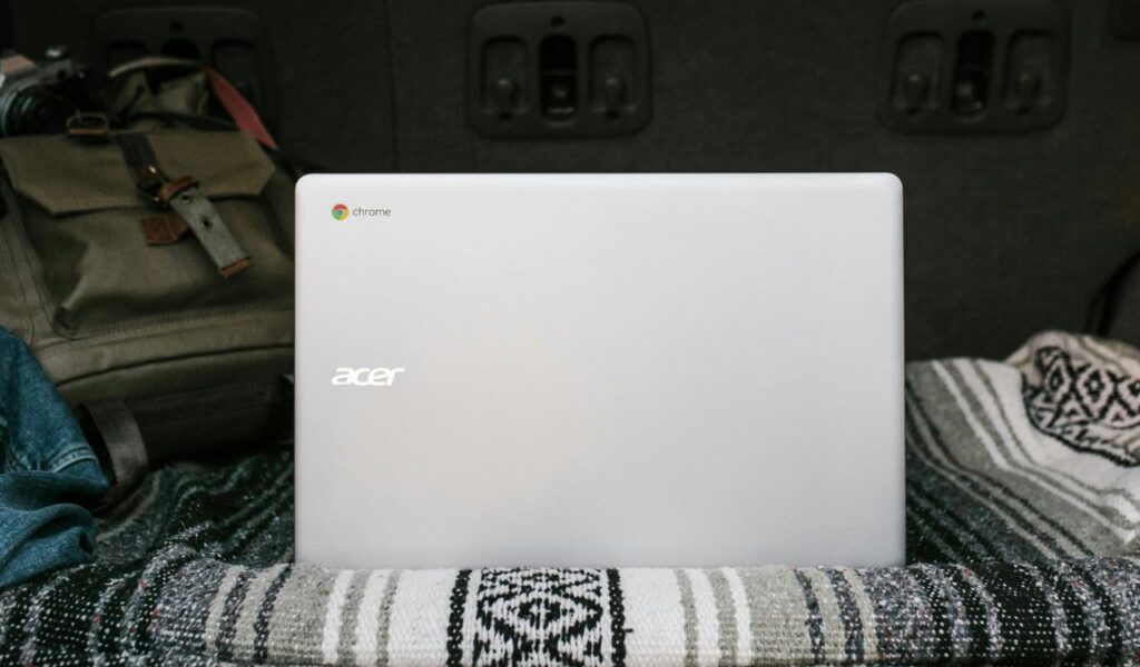 A closed Acer Chromebook laptop placed on a blanket with a backpack in the background